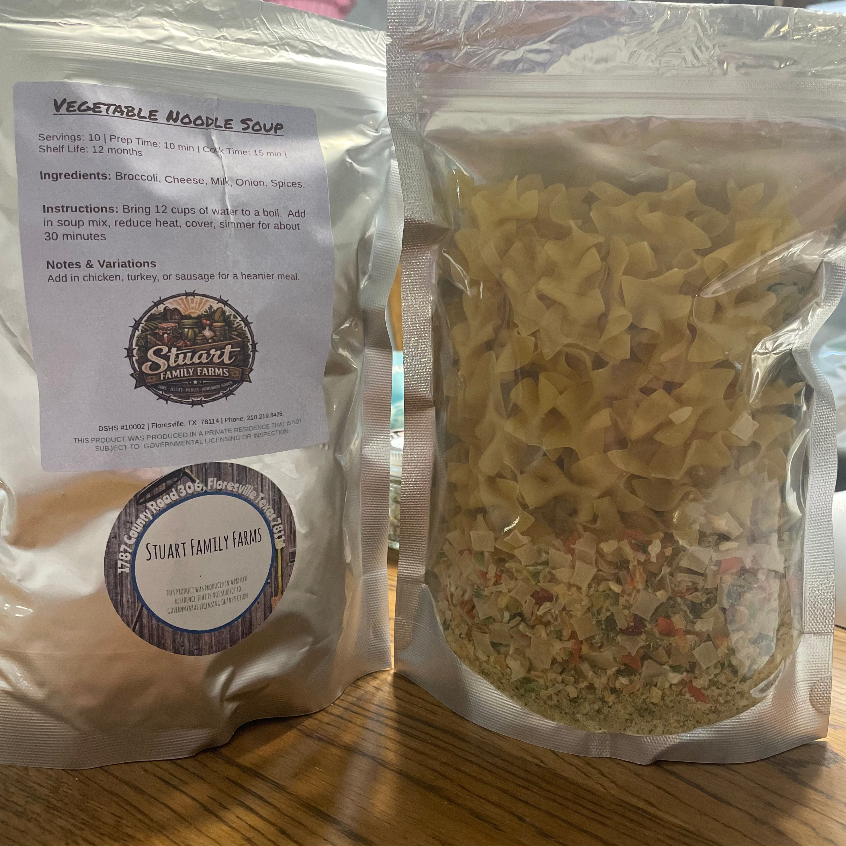 Two packages of Stuart Family Farms vegetable noodle soup on a wooden surface.